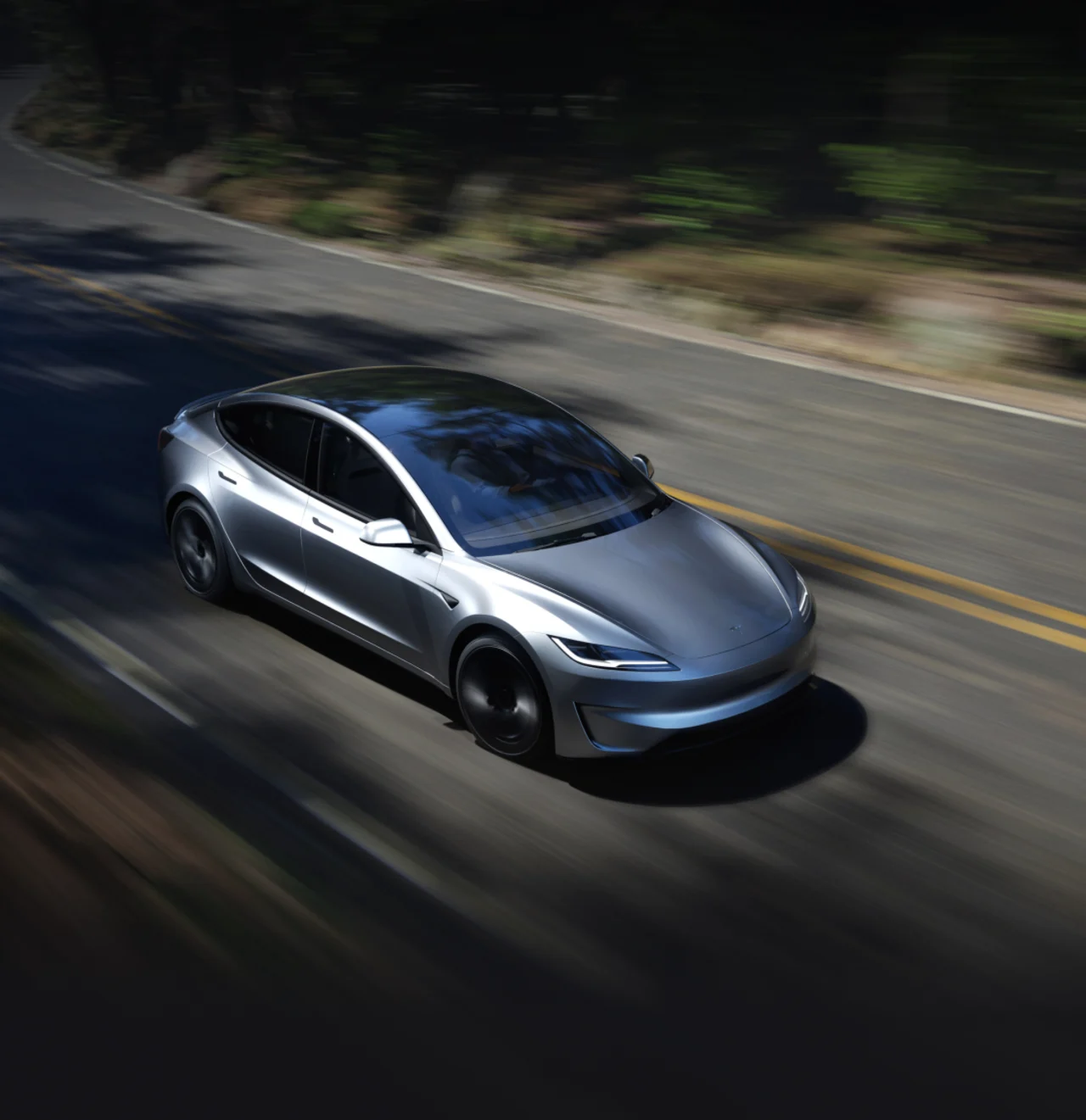 Silver Tesla Model 3 driving on a forest road